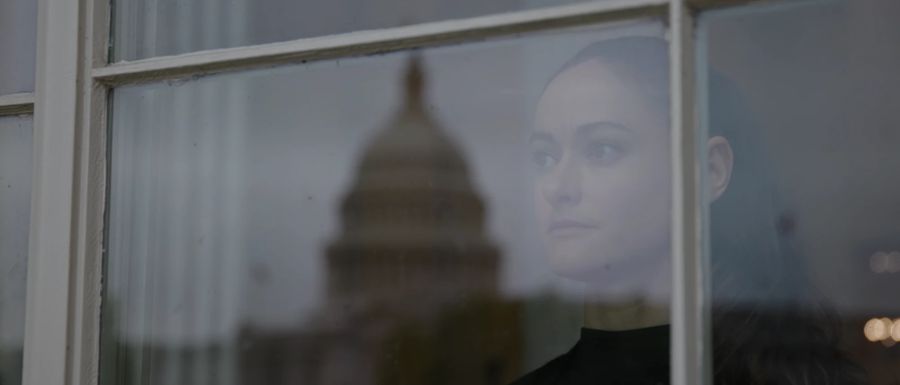 A woman looks out a window, the Capitol dome reflected in the glass