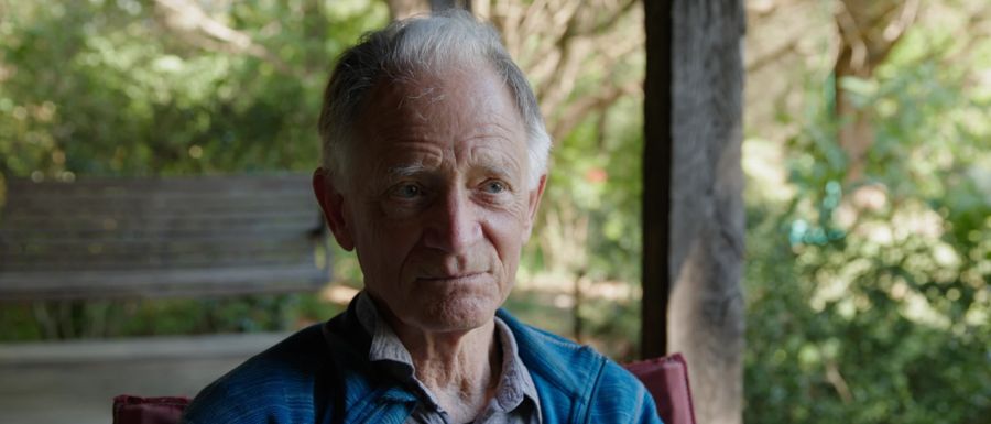 An older man interviewed on a shaded porch