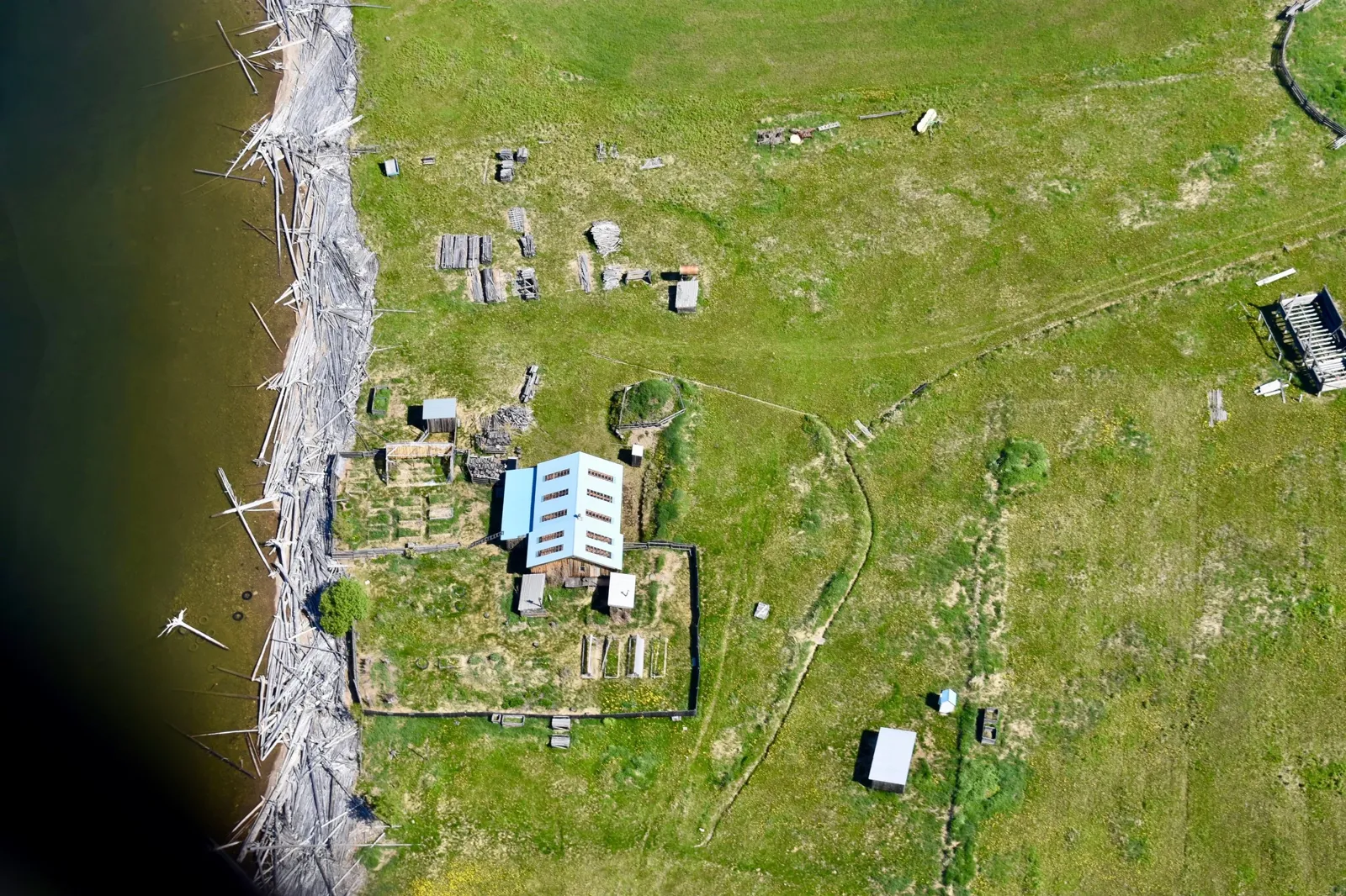 Aerial view of a settlement on green land beside a river shore lined with driftwood