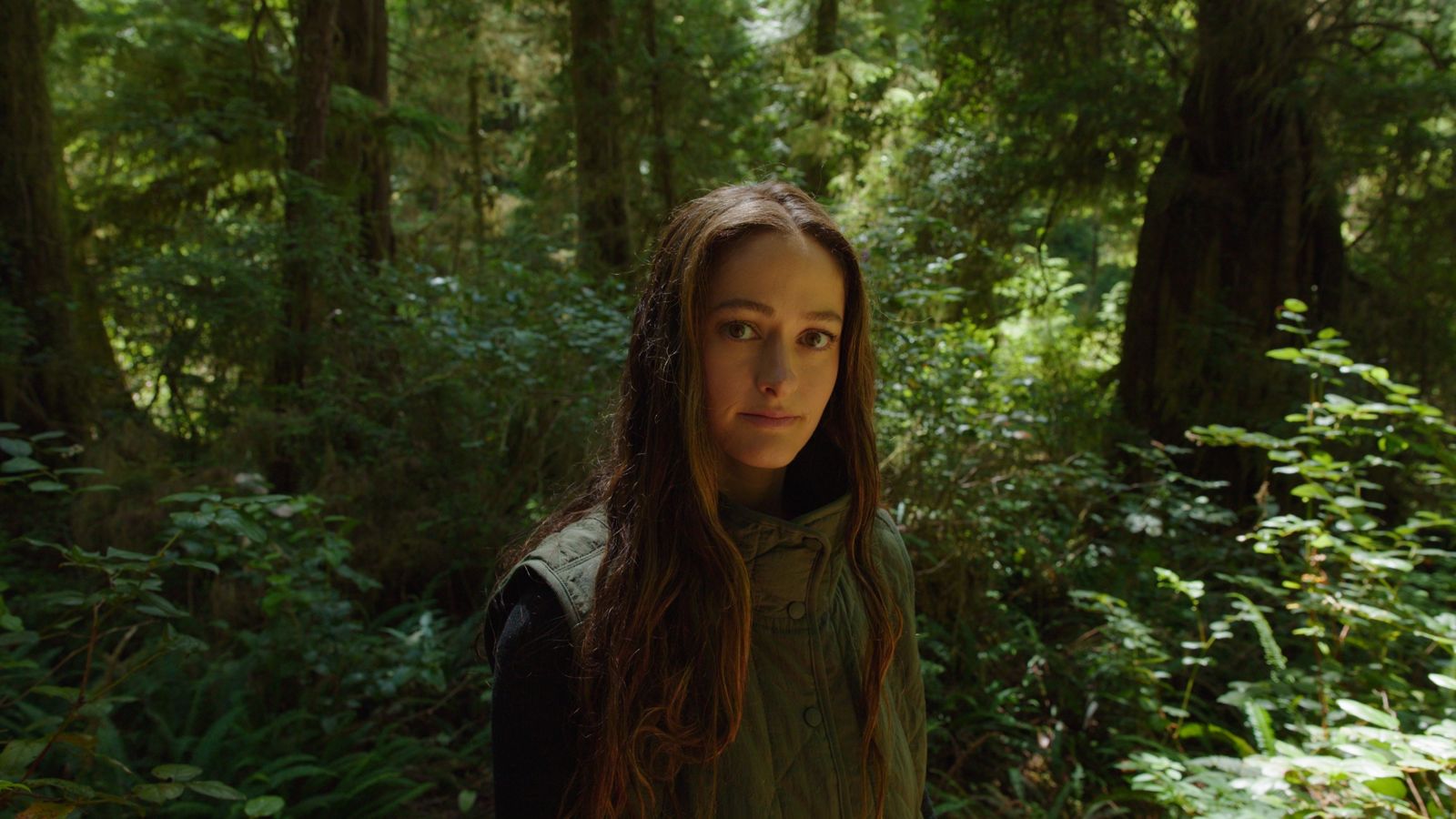 Maia Wikler in a green vest among old-growth trees and salal in a coastal rainforest