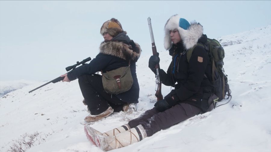 A mother and daughter rest on a snowy slope holding rifles