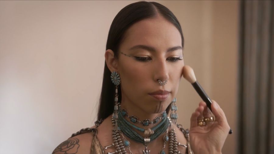A young woman in turquoise jewelry has her makeup done