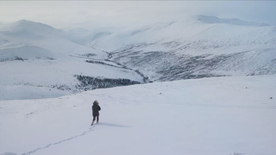 A lone figure in a parka walks across snow-covered hills
