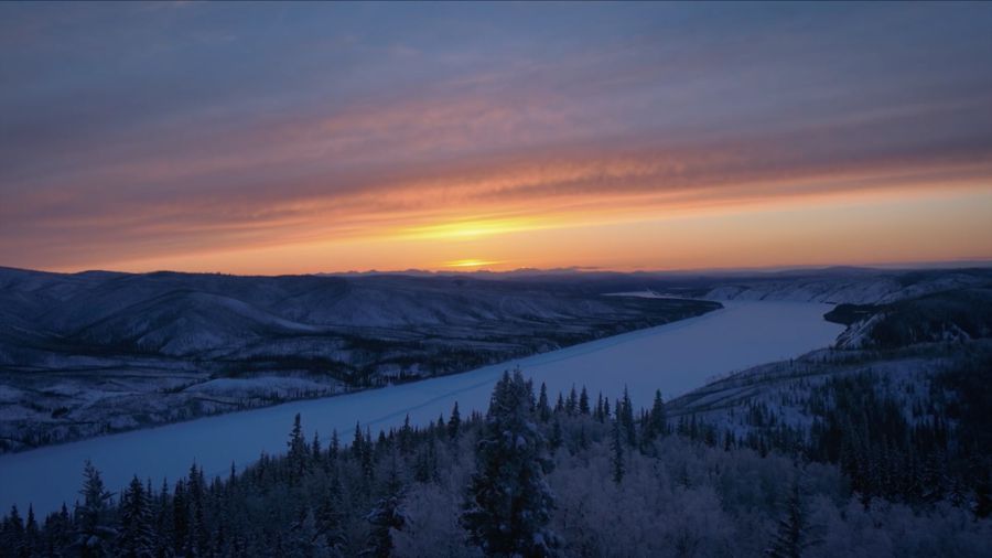Sunset over a frozen river winding through snowy hills