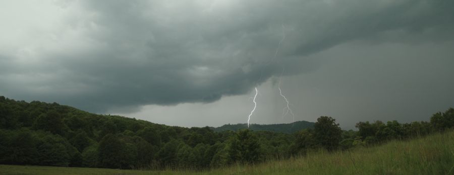 Lightning under storm clouds over forested hills